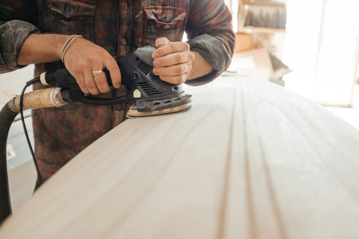 Een vakman schuurt een lichte houten plank met een schuurmachine
